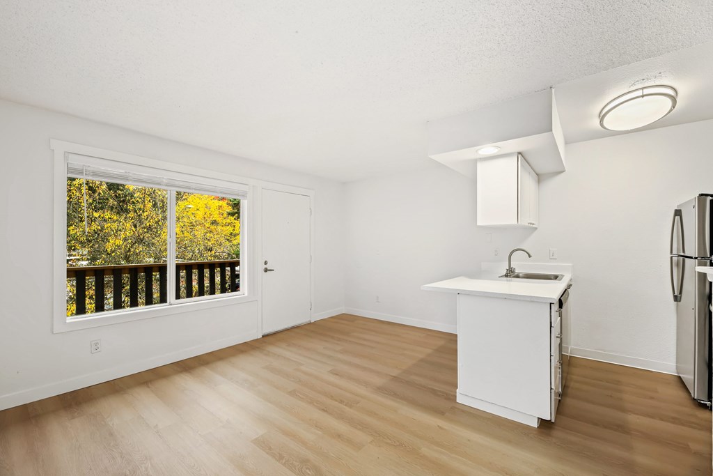 A kitchen with a white fridge and a window with a view of trees.