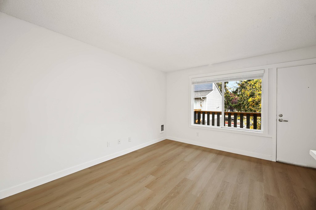 A room with a white door and a window showing a balcony with a white house and trees in the background.