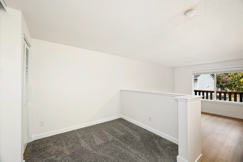 A room with a carpeted floor and a window with a view of a balcony.