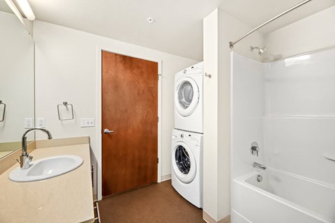 A bathroom with a white tub, sink, and washer and dryer.
