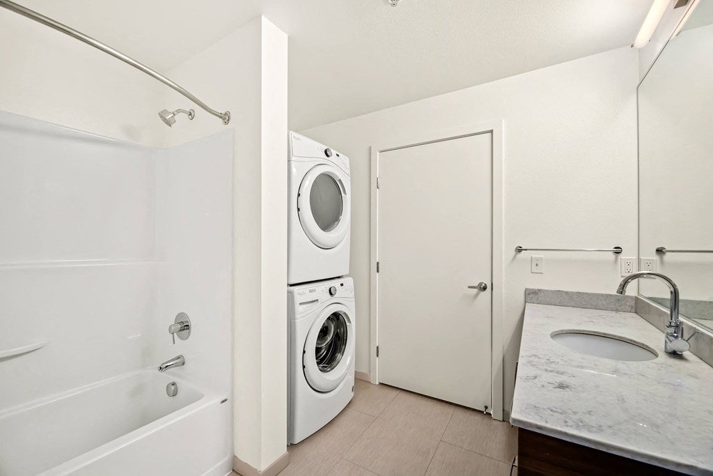 A white bathroom with a tub, sink, and washer and dryer.