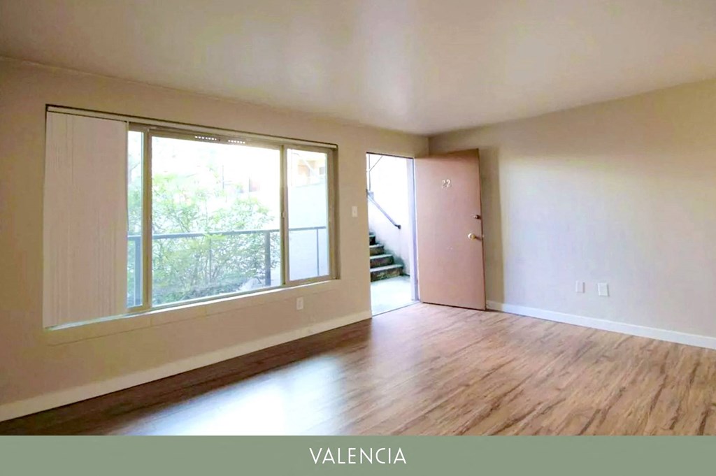 an empty living room with a large window and wooden floors