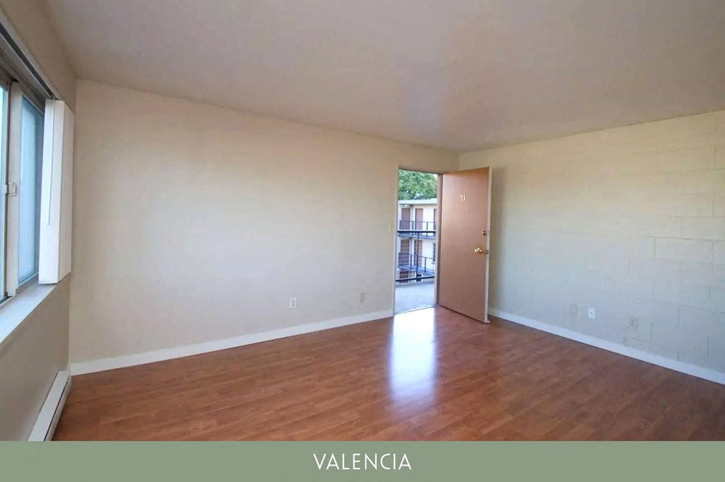an empty living room with wood flooring and a door to a balcony