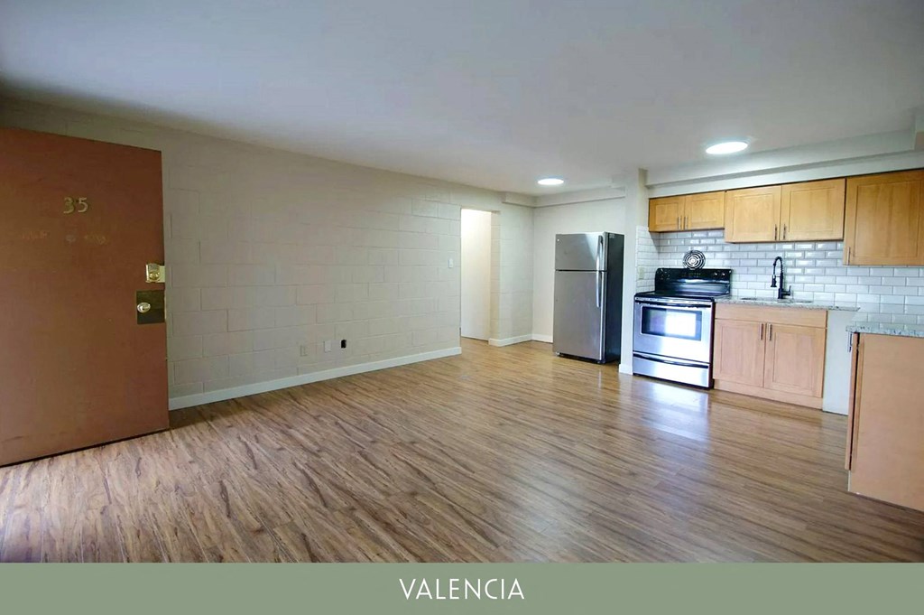 an empty living room with wooden floors and a kitchen with a stove and refrigerator