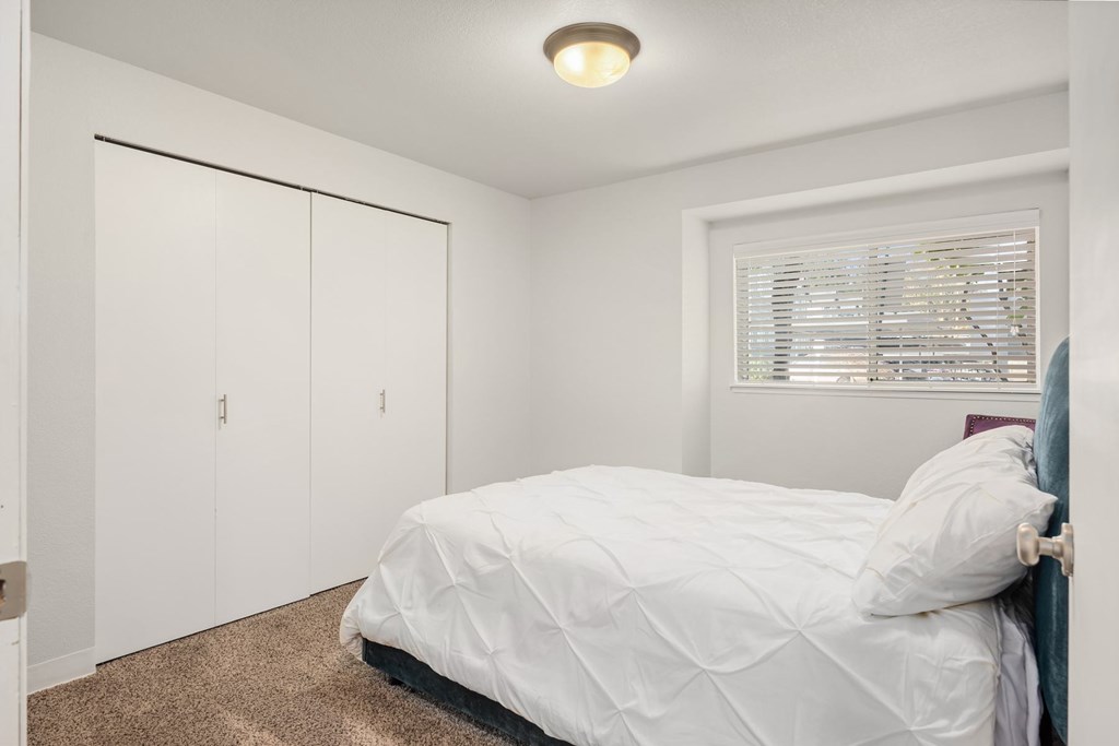 A bedroom with a bed, two closets, and a window with blinds.