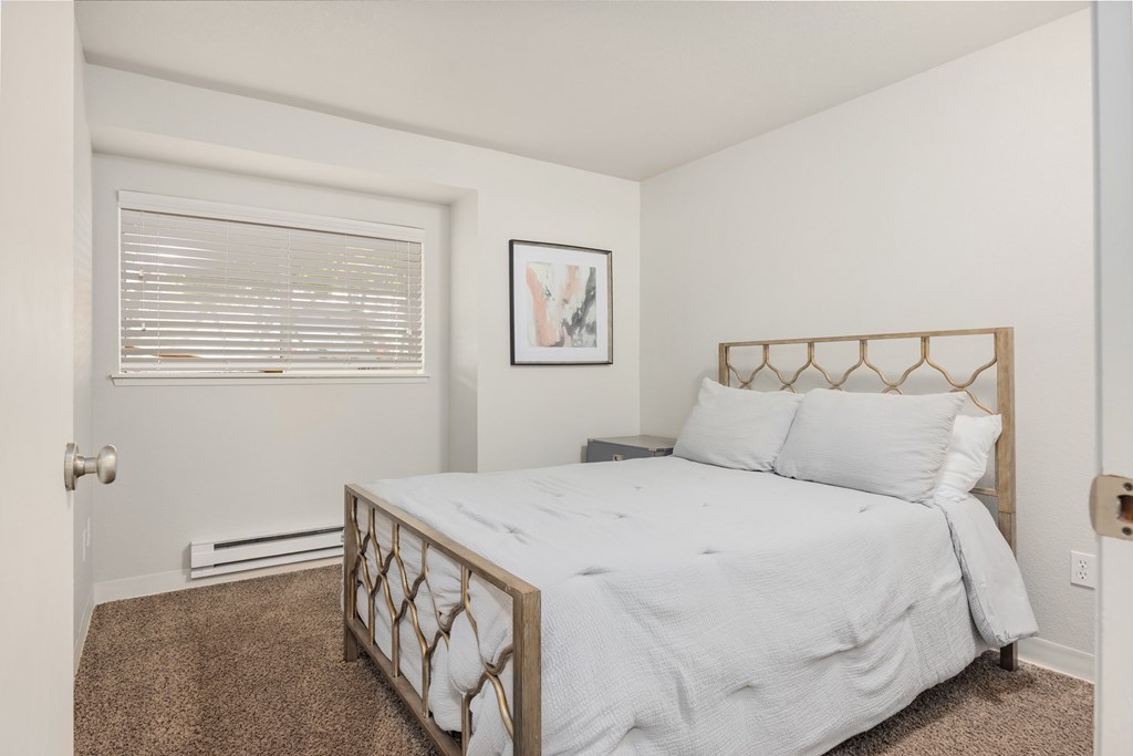 A bedroom with a bed, pillows, and a picture on the wall.