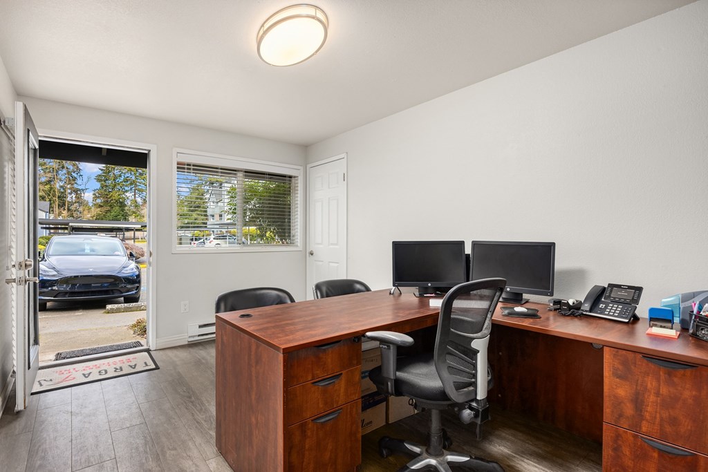 A room with a desk and chairs with a door open to a balcony.
