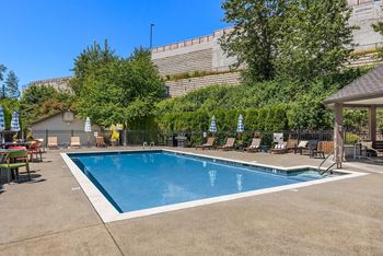 a swimming pool with chairs and tables around it in front of a building