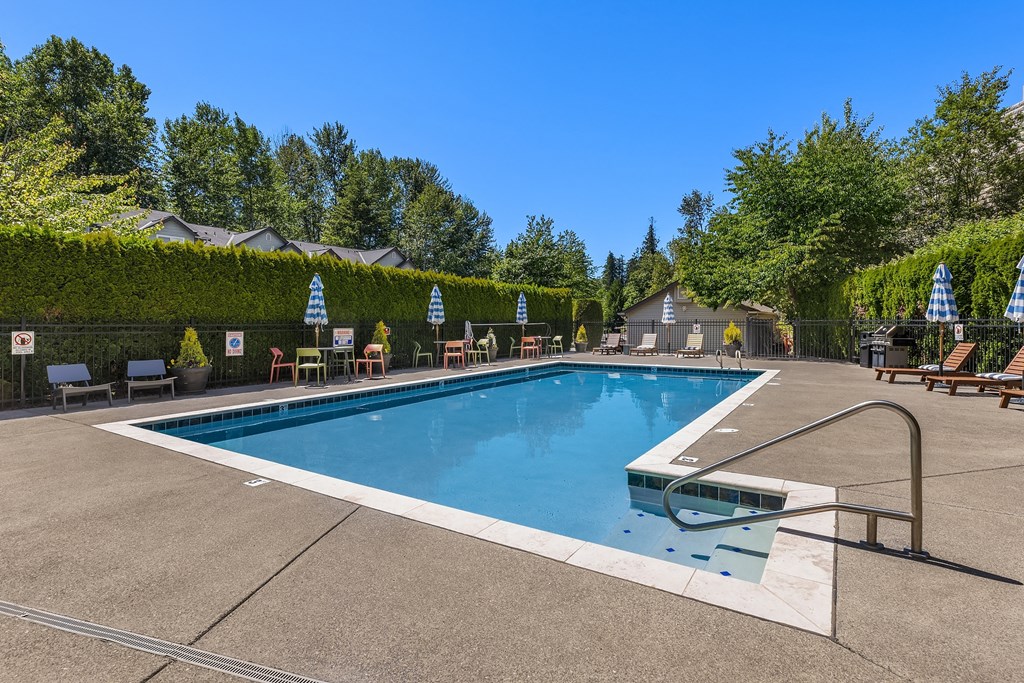 a swimming pool with chairs around it and trees in the background
