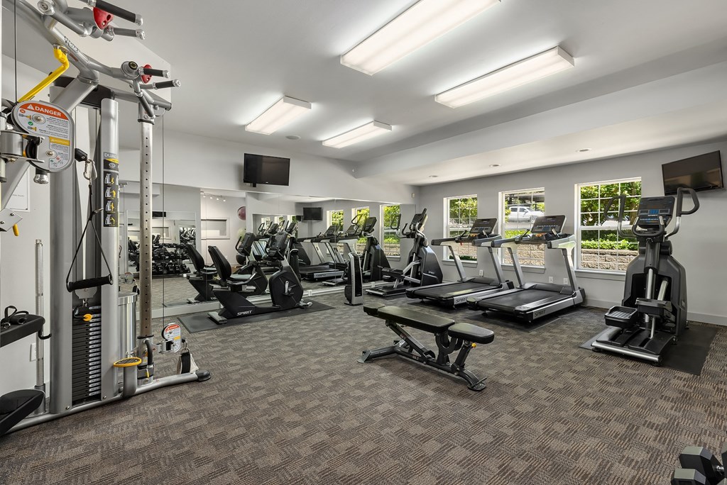 a gym with cardio equipment and weights in a room with windows