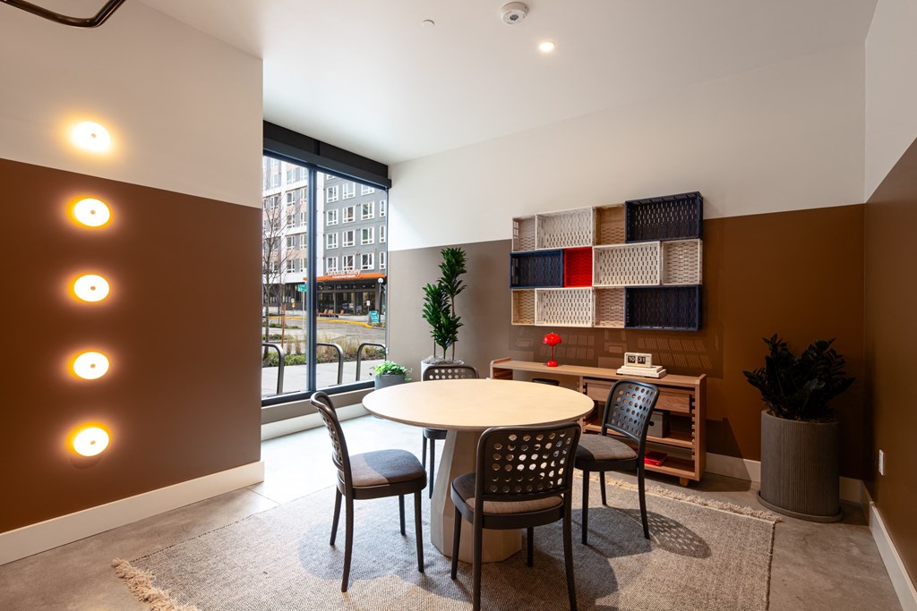A room with a round table and chairs, a potted plant, and a shelf with a red and white object on it.