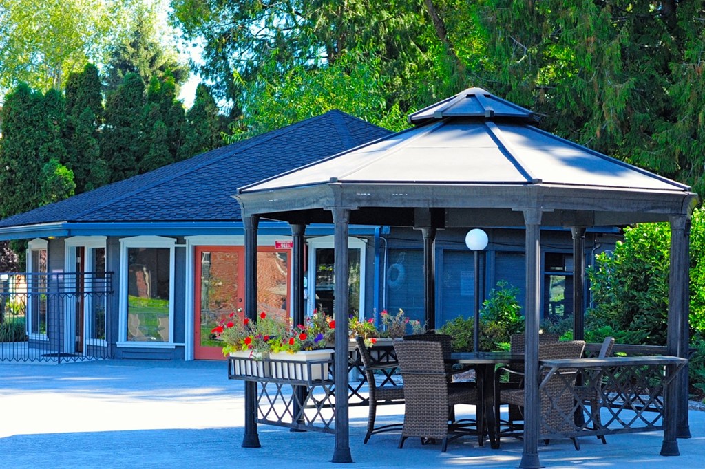 a gazebo with a table and chairs in front of a house
