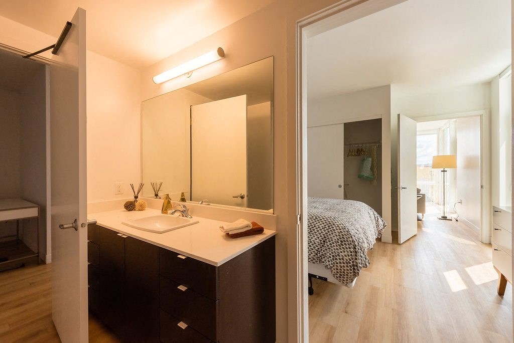 a bathroom with a sink next to a mirror and a bedroom in the background