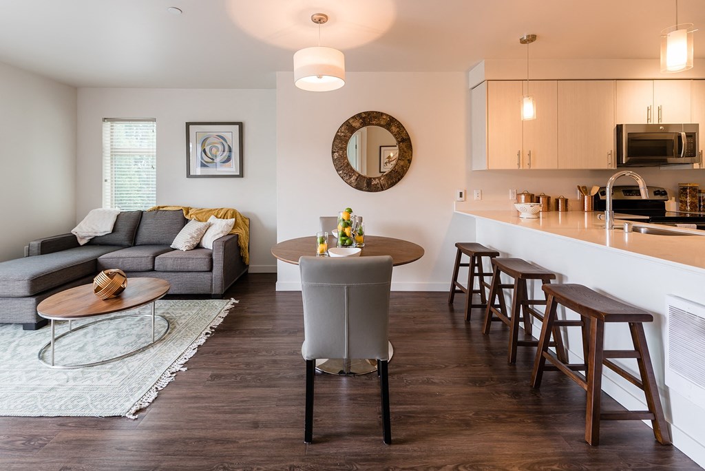 a living room and kitchen area with white walls and wood flooring