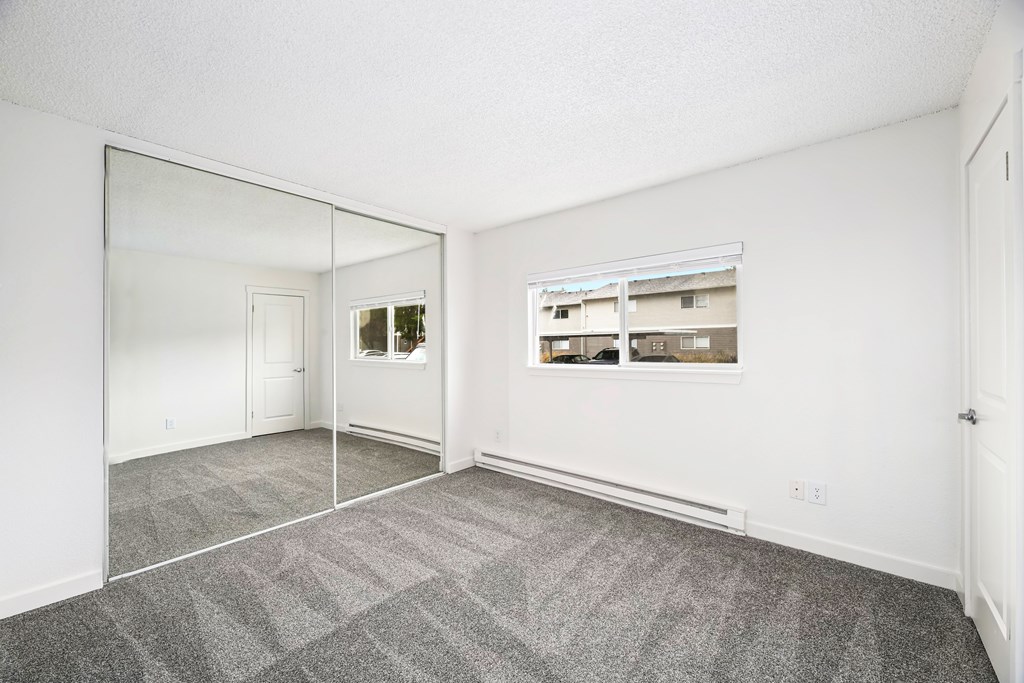 A large empty room with a grey carpet and a mirror on the wall.