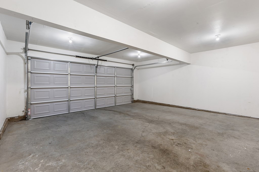 A large, empty garage with a white wall and a grey floor.