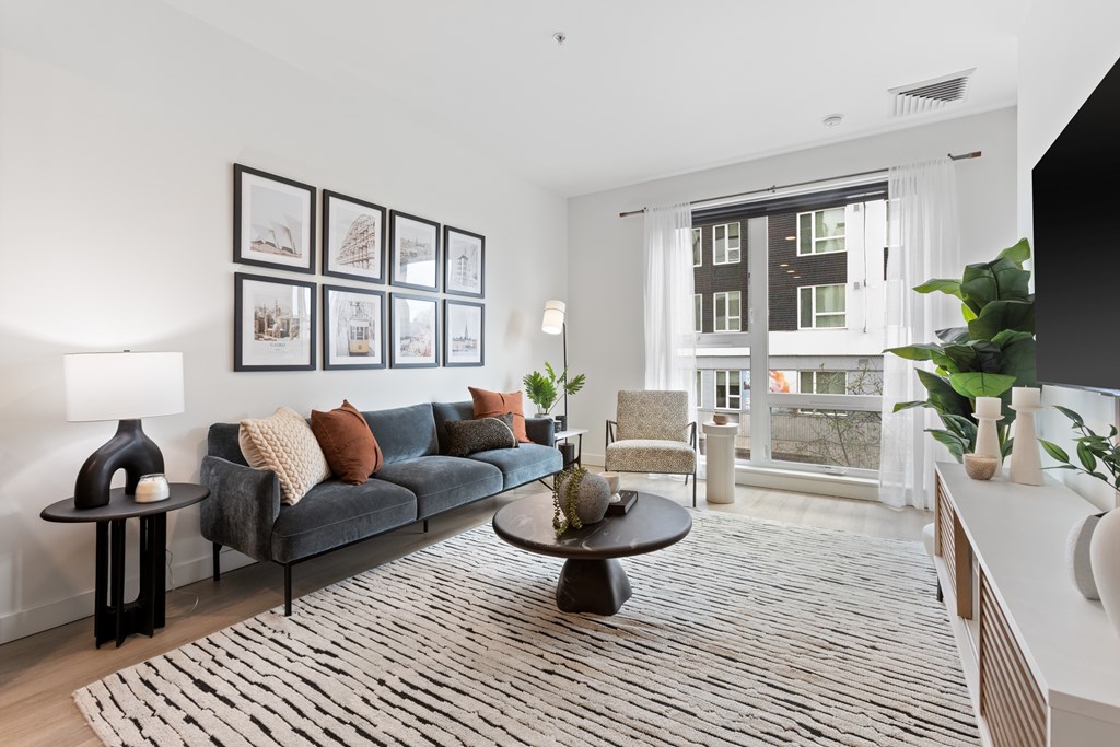 A living room with a grey couch, a coffee table, and a large window.