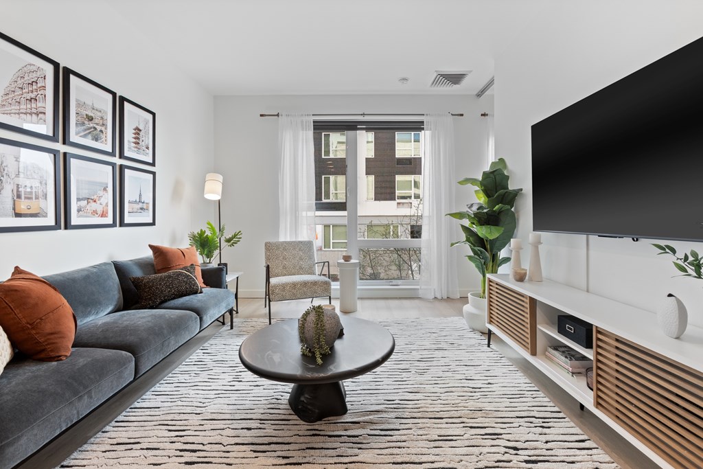 A living room with a grey couch, a black coffee table, and a large window with a view of a building outside.