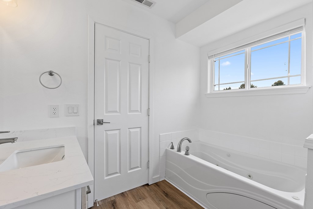 A white bathroom with a tub, sink, and window.