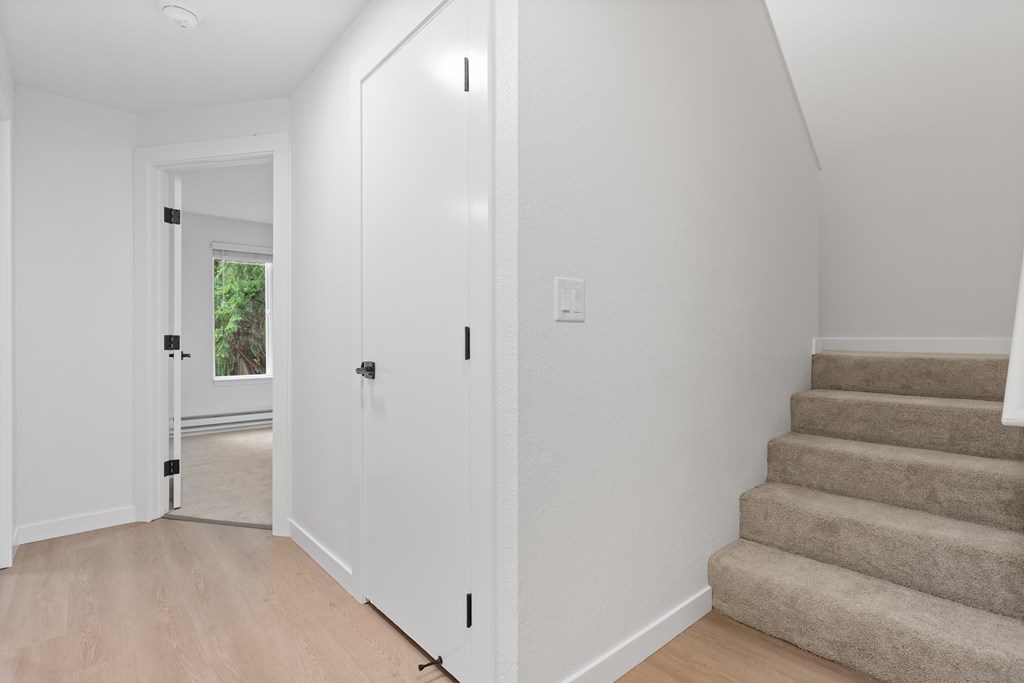 A hallway with a staircase and a door leading to a balcony.