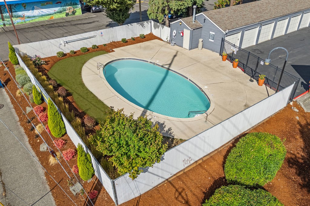 A small pool surrounded by a white fence and green bushes.
