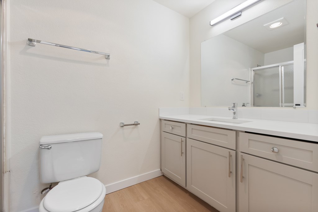A white toilet sits in a small bathroom with a sink and mirror.