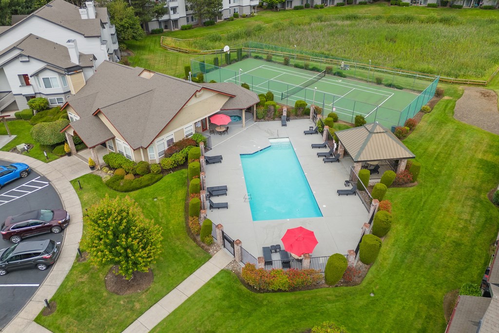 A tennis court is surrounded by a pool and a small building.