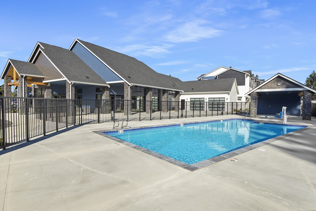 A large swimming pool is surrounded by a black fence and a building with a grey roof.