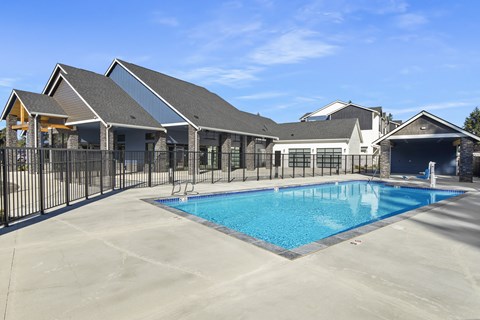 A large swimming pool is surrounded by a black fence and a building with a grey roof.