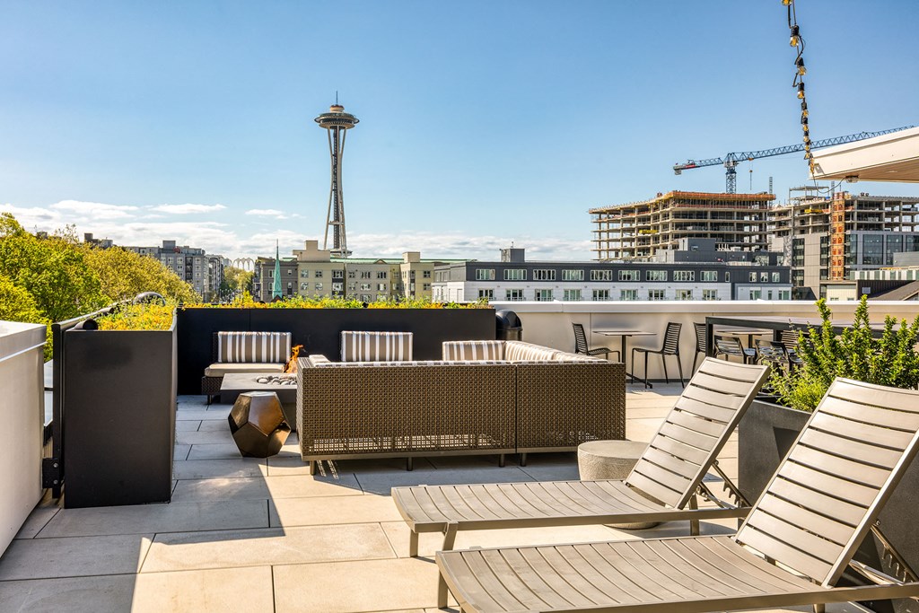 a rooftop patio with chairs and tables and a city in the background