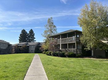 A walkway leads to a building with a porch and a tree in front.