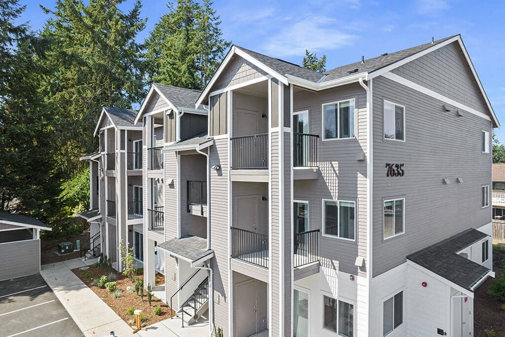 Apartment building with balconies and a parking lot in front.