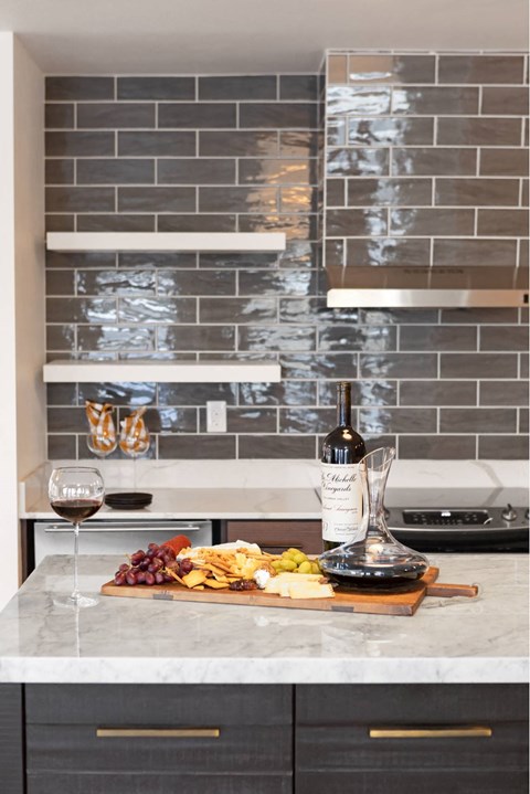 A kitchen counter with a wine bottle, glass, and a plate of food.