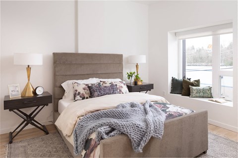 A bedroom with a bed covered in a grey blanket and a grey headboard.