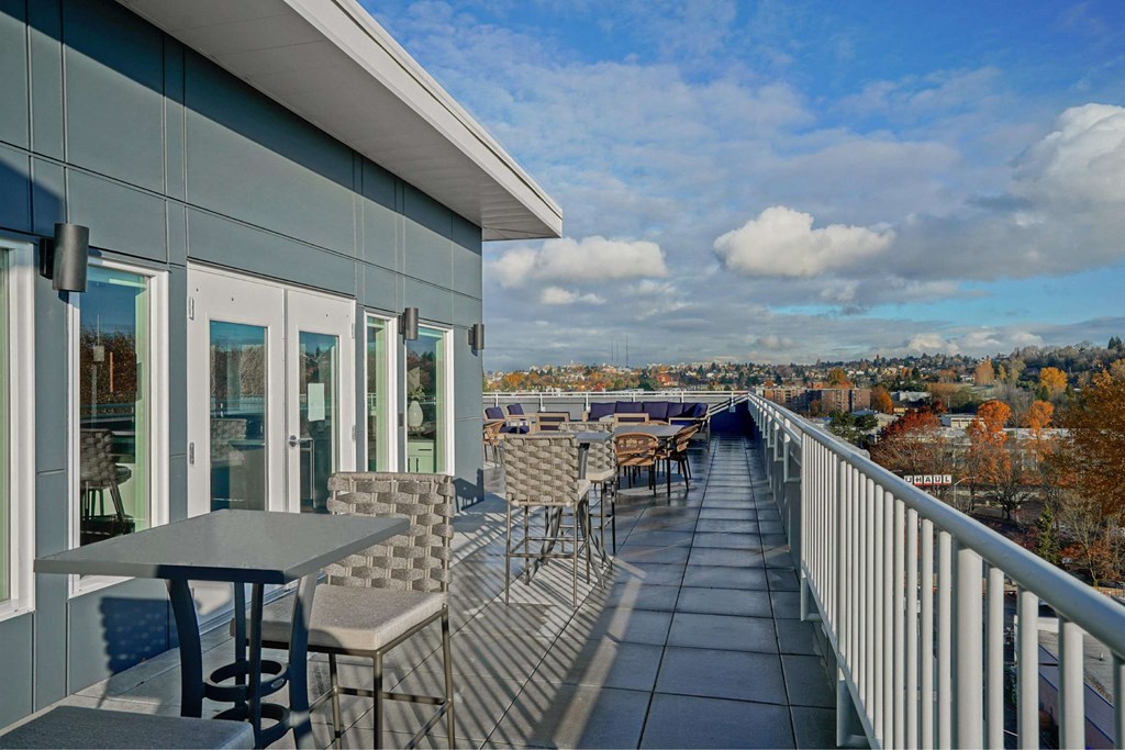 A rooftop deck with tables and chairs, overlooking city and mountains