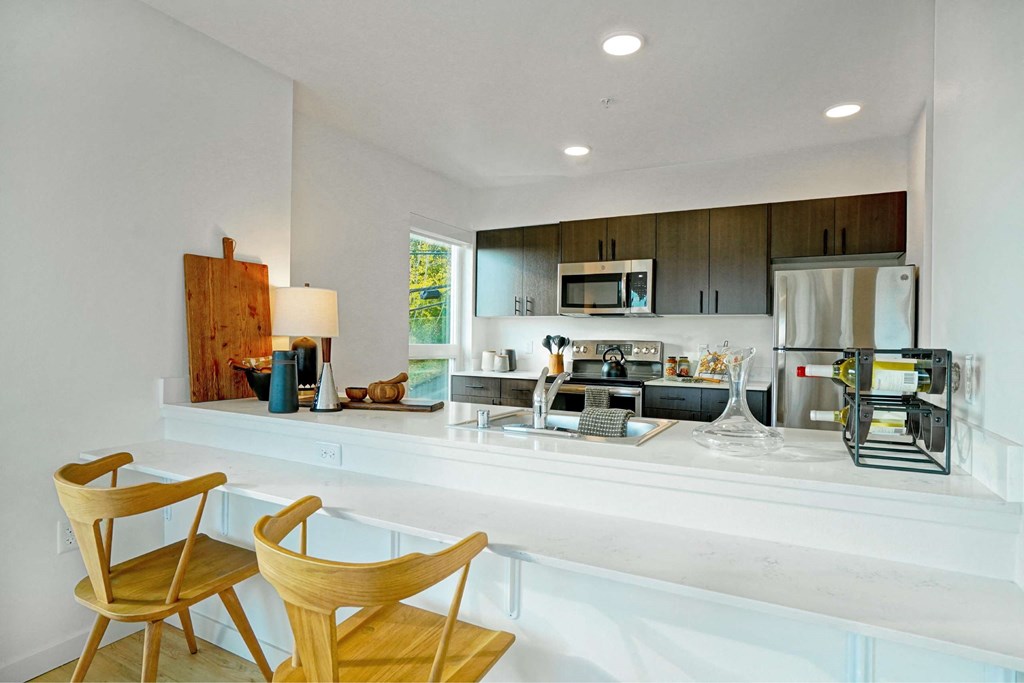 A modern kitchen with wooden chairs and white countertops.