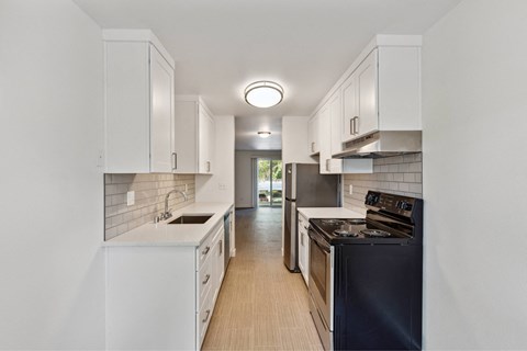 A modern kitchen with white cabinets and a black stove top oven.