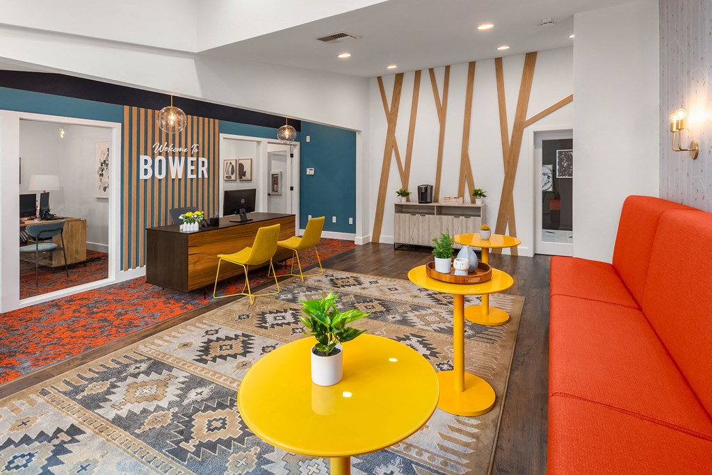 a lobby with orange couches and yellow tables and a blue wall with a sign