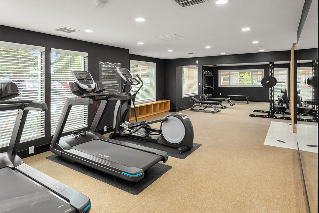 a gym with treadmills and other exercise equipment in a room with windows