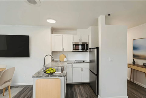 A modern kitchen with white cabinets and a black television mounted on the wall.