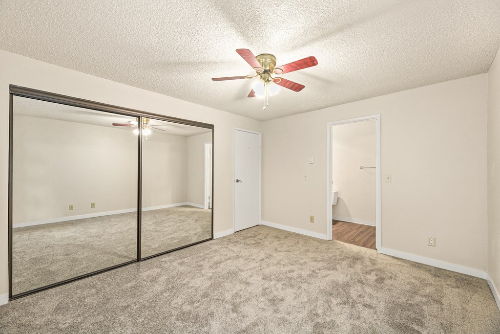 an empty living room with a ceiling fan and a mirrored closet