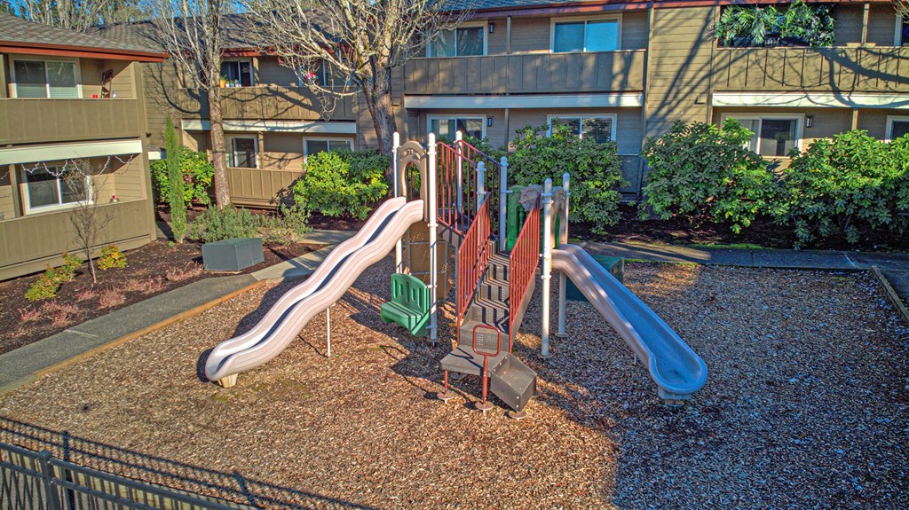 a playground with slides and chairs in front of an apartment building
