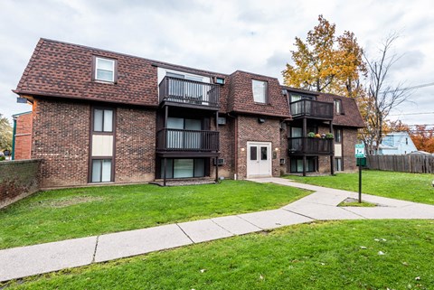 A brick building with a balcony and a green lawn in front.