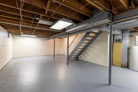 A spacious attic room with a staircase and exposed wooden beams.