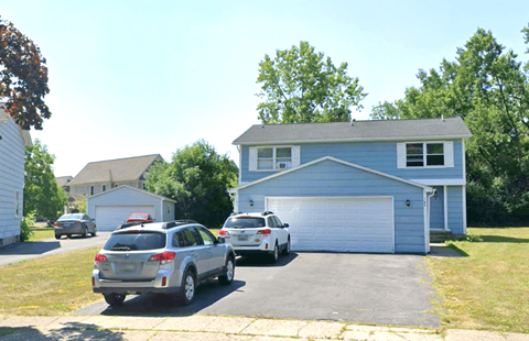 A silver SUV is parked in front of a blue house.