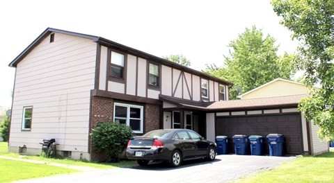 A black car is parked in front of a house with a garage.