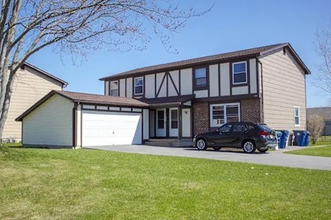 A black car is parked in front of a two-story house.