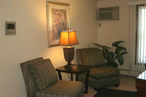 A living room with a striped chair and a table with a lamp on it.