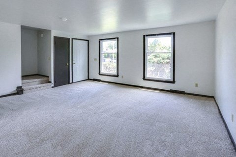 A spacious room with grey carpeting and three windows.