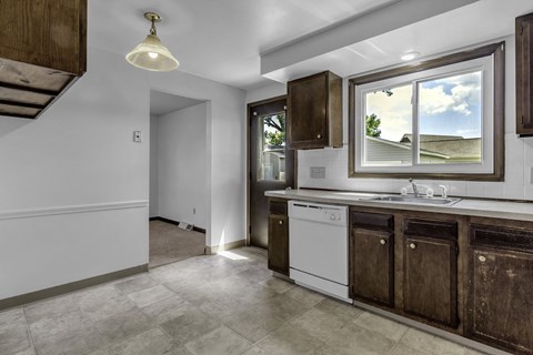 A kitchen with a white dishwasher and dark brown cabinets.